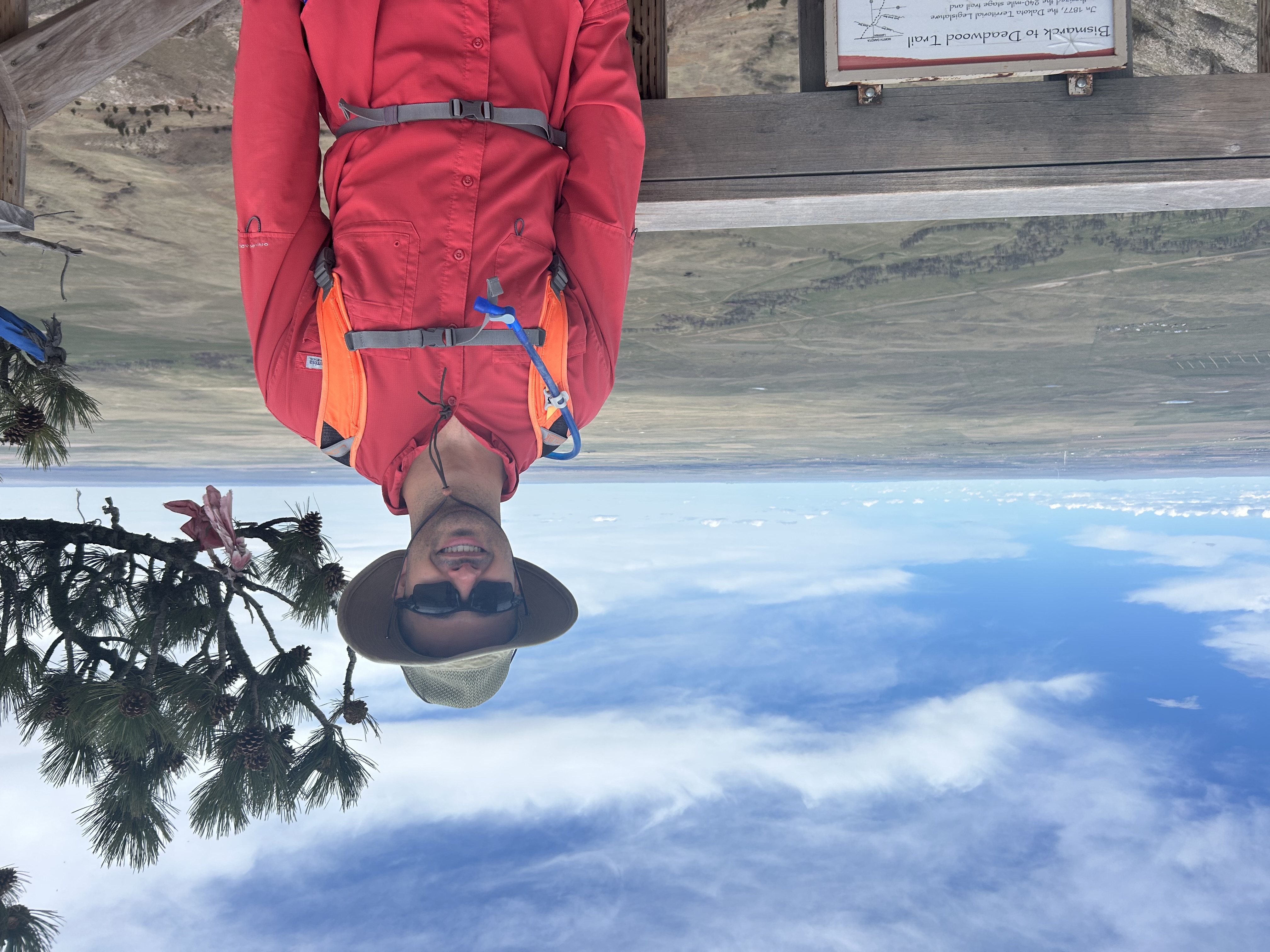 Dr. Alexander Reid at the top of Bear Butte, SD, wearing a wide-brimmed sun hat, close-fitting sunglasses, and a long-sleeved sun shirt