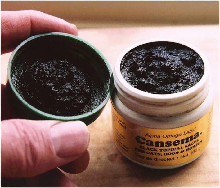 A jar of Alpha Omega Labs' Cansema black topical salve, opened to show the dark tarry paste inside