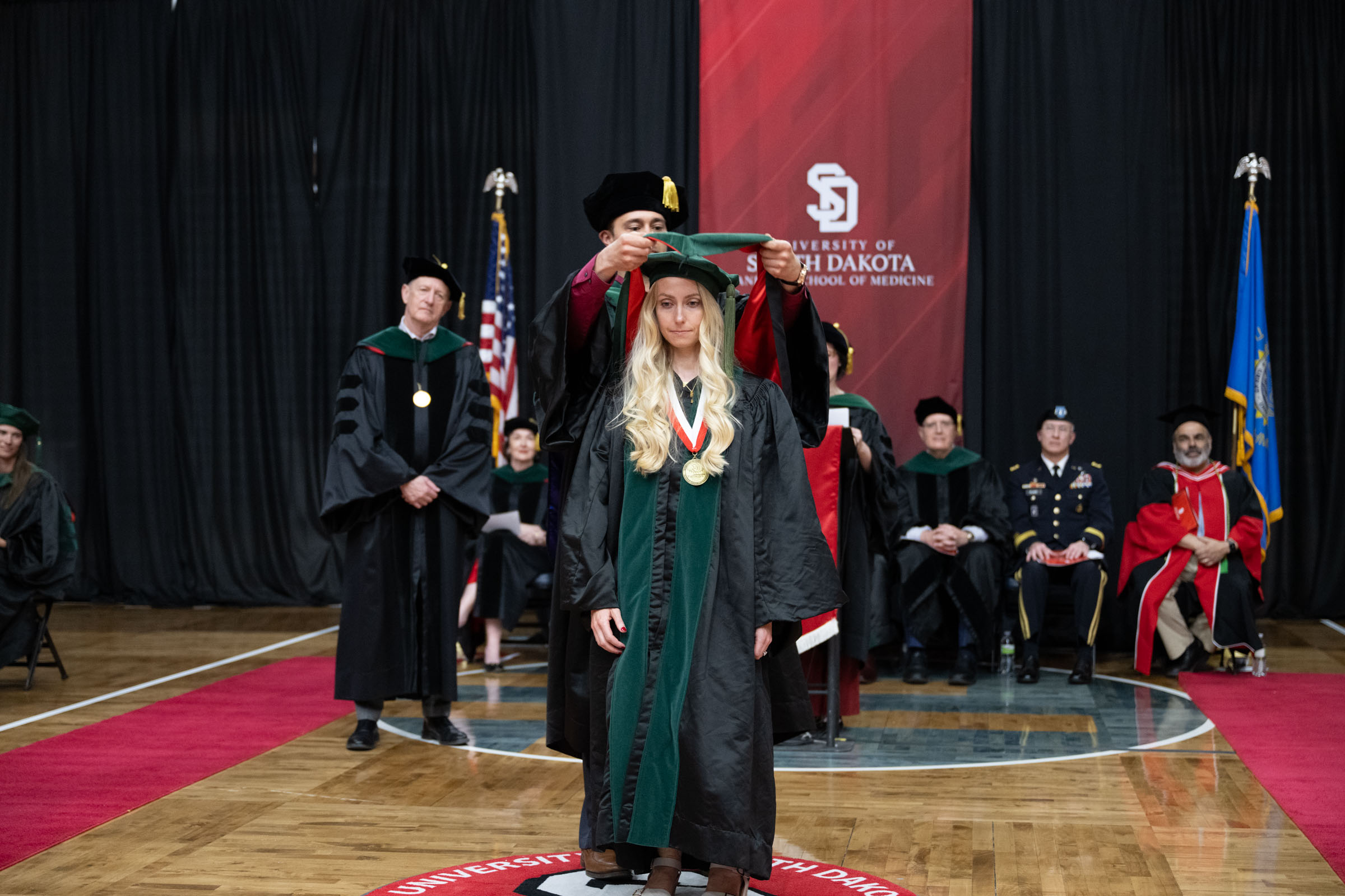 Dr. Alexander Reid placing the doctoral hood on his sister Elise on stage at the University of South Dakota Sanford School of Medicine commencement