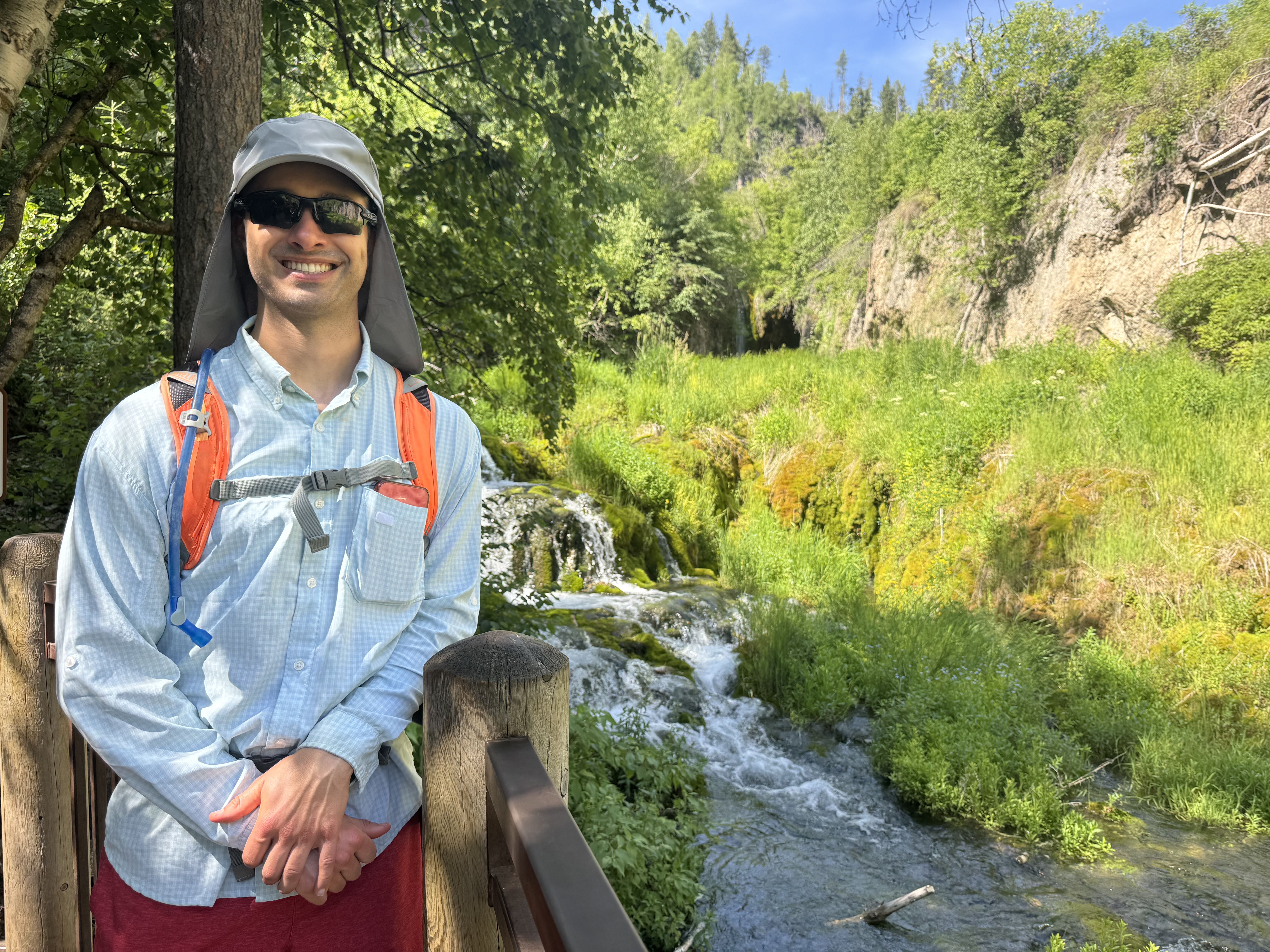 Dr. Alexander Reid at Roughlock Falls in Spearfish Canyon wearing a UPF long-sleeved shirt, wide-brimmed sun hat, and UV-blocking sunglasses