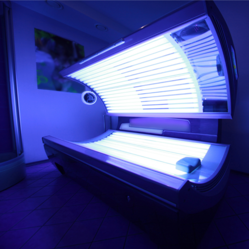 An open indoor tanning bed glowing blue-violet in a salon room